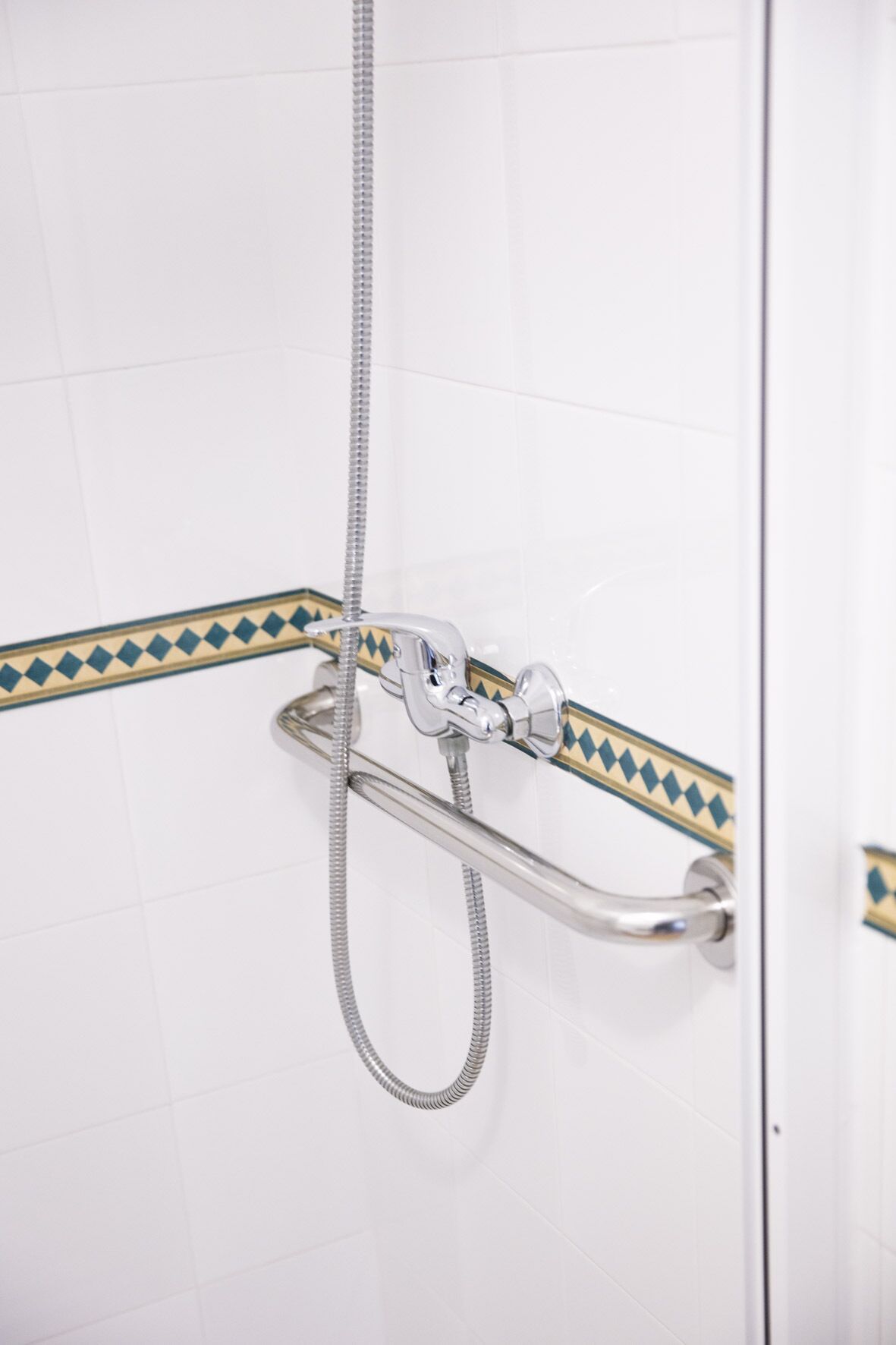 A shower with a handheld showerhead and a fixed showerhead, both mounted on a wall with a decorative border.