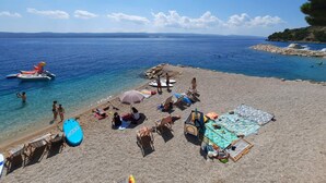 A beach with clear blue water, a rocky shoreline, and a few people enjoying the sun. - Villa Carica (Omis)