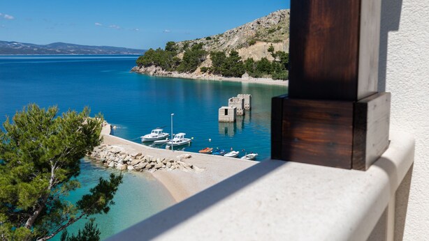 A coastal view with boats docked at a pier, a rocky shoreline, and a clear blue sea. - Villa Carica (Omis)