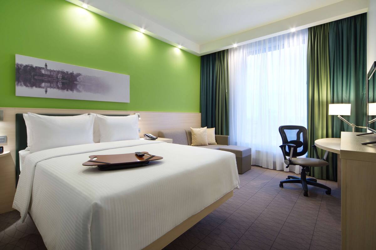 Ein Hotelzimmer mit einem großen Bett, einem Schreibtisch mit Stuhl, einem Telefon und einem Bild an der Wand.