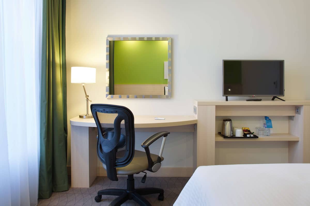 Ein Hotelzimmer mit Bett, Schreibtisch mit Stuhl, Fernseher und Ablage für Annehmlichkeiten.