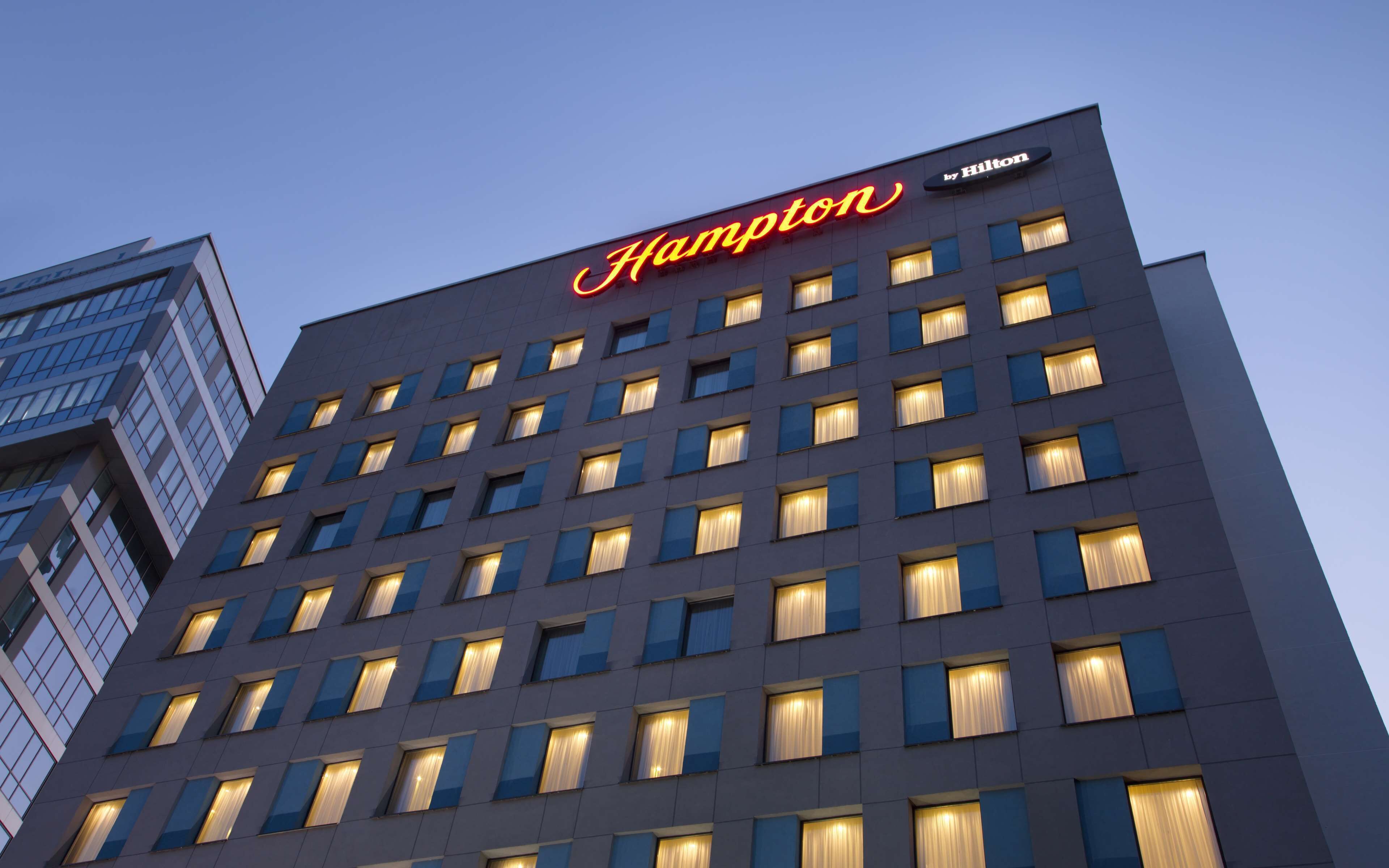 A hotel building with a prominent 'Hampton' sign, multiple windows, and a modern architectural design.