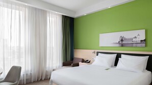 Een hotelkamer met een groot bed, een stoel, een bureau met telefoon en een schilderij aan de muur.