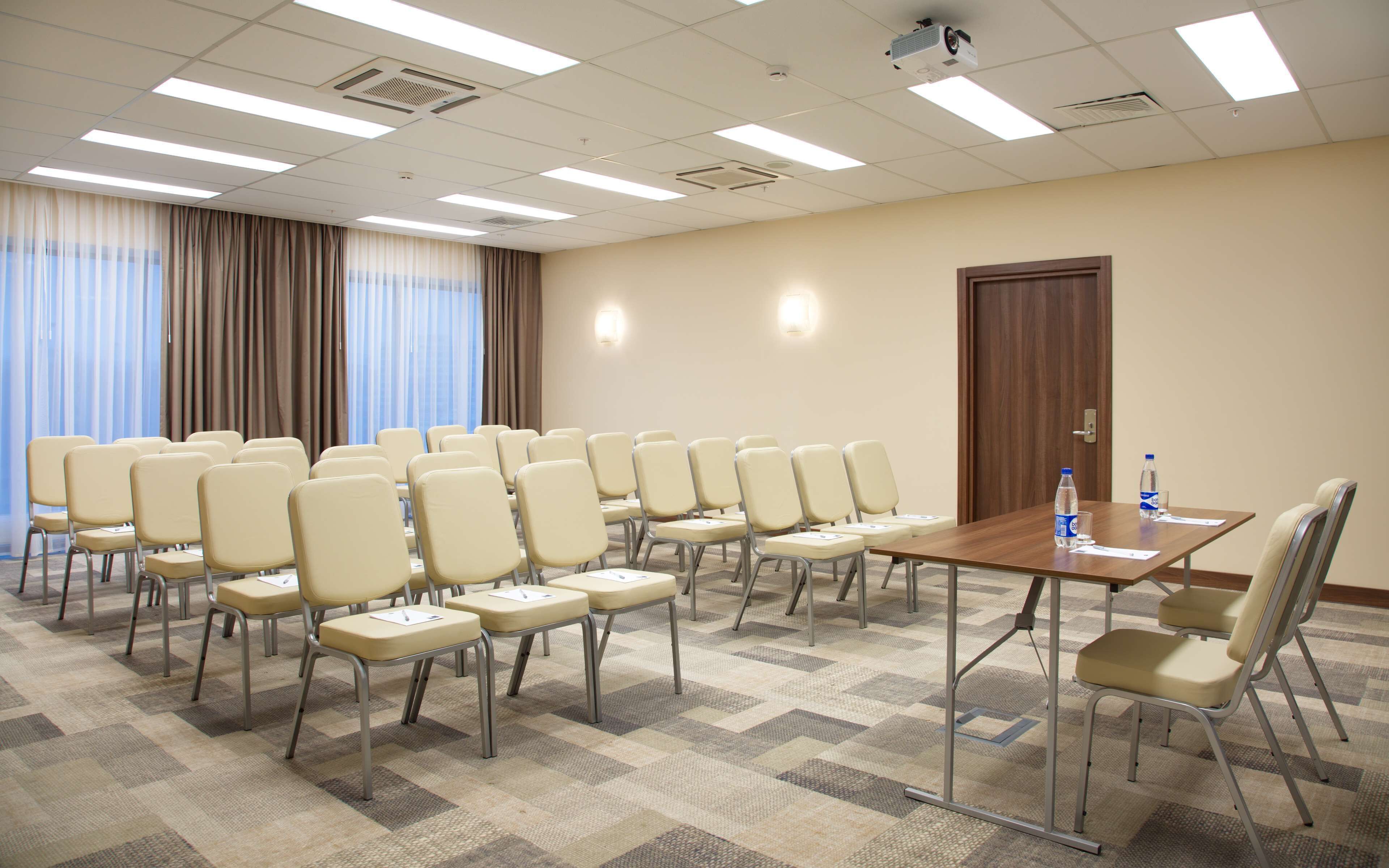 A conference room with rows of chairs, a table with water bottles, and a projector on the ceiling.