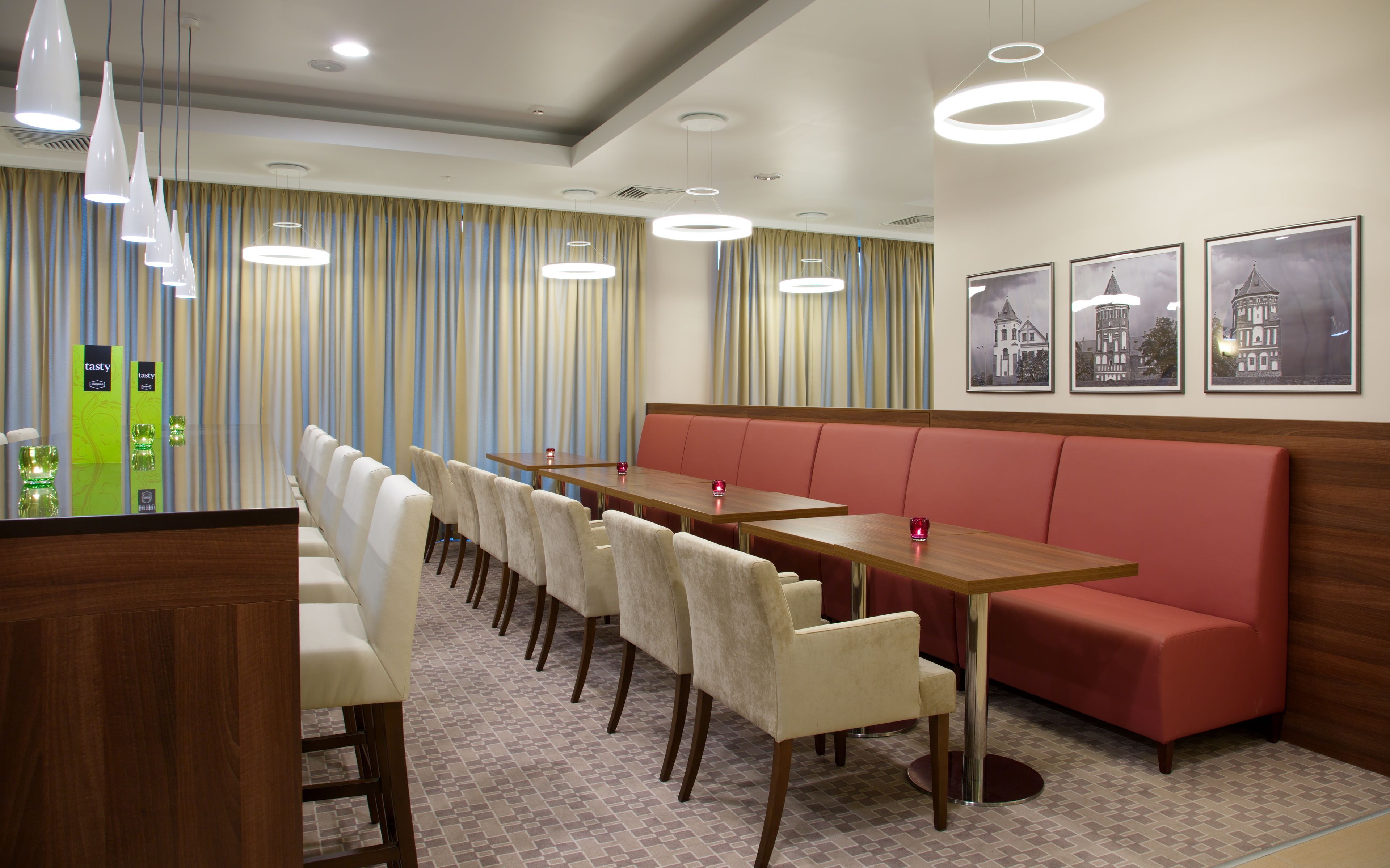 A hotel dining area with a long wooden table, beige chairs, a red booth, and striped curtains.
