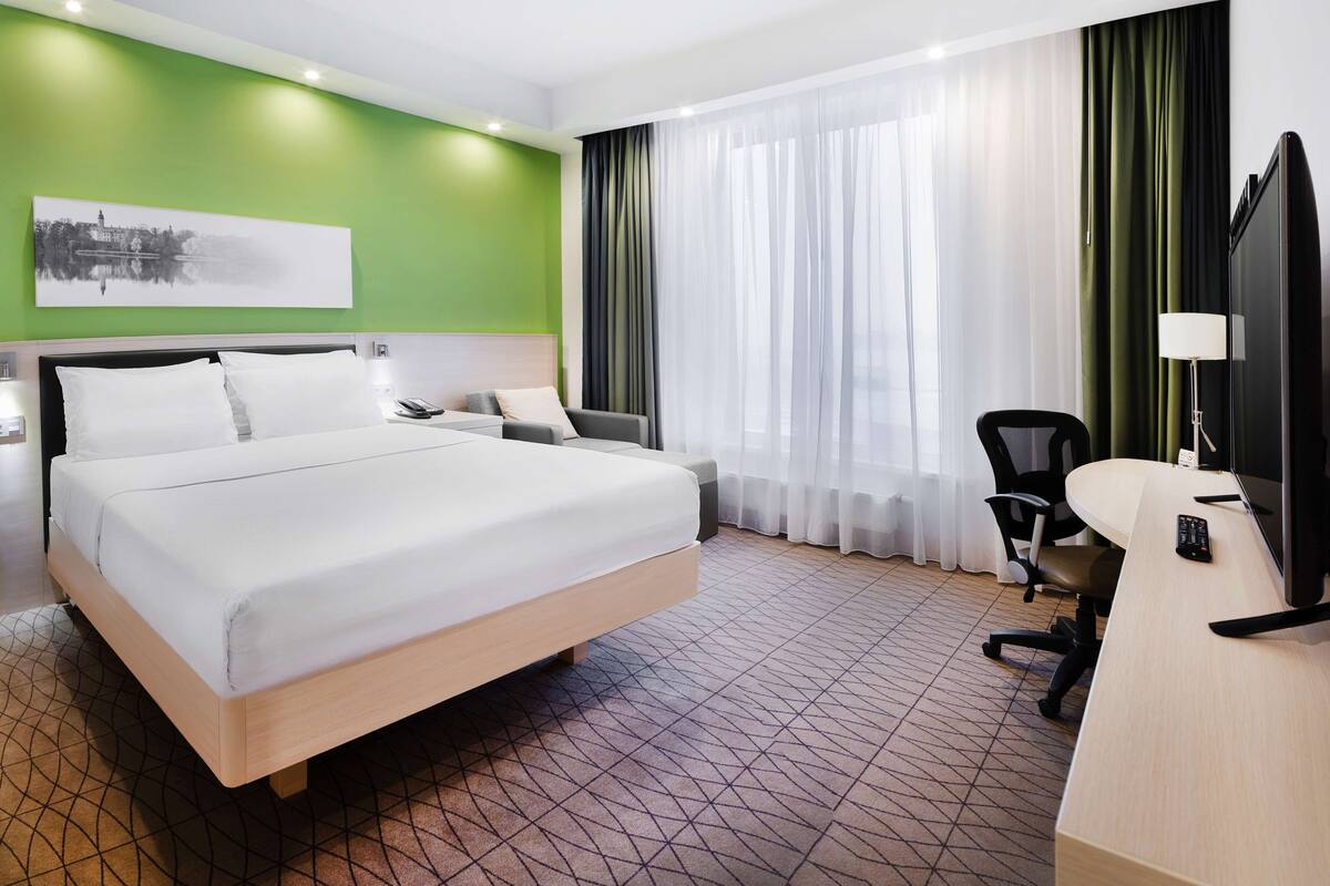 Ein Hotelzimmer mit einem großen Bett, einem Schreibtisch mit Computer und einem Sessel.