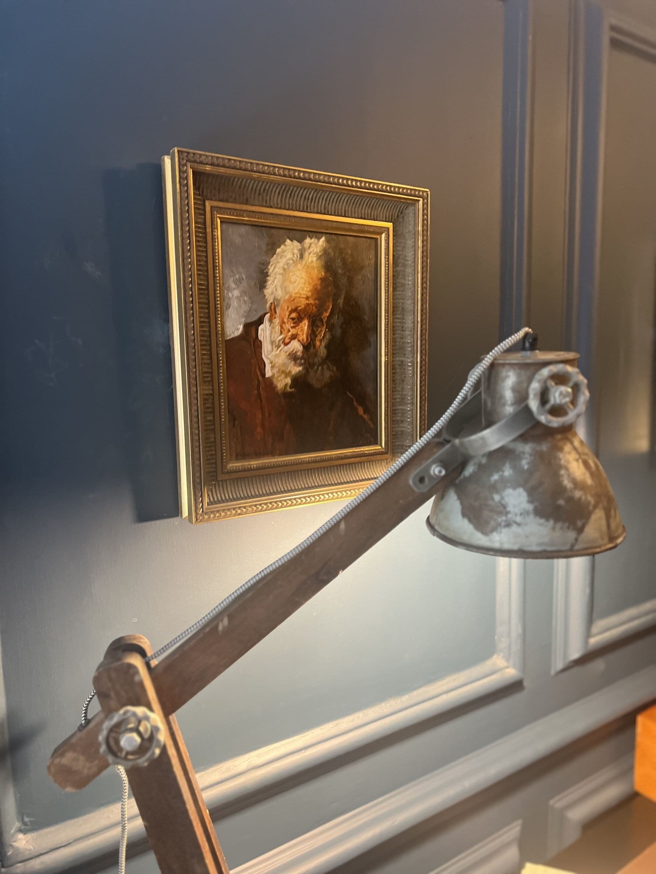 Un portrait encadré accroché au mur, une lampe de bureau ancienne et un crucifix en bois.