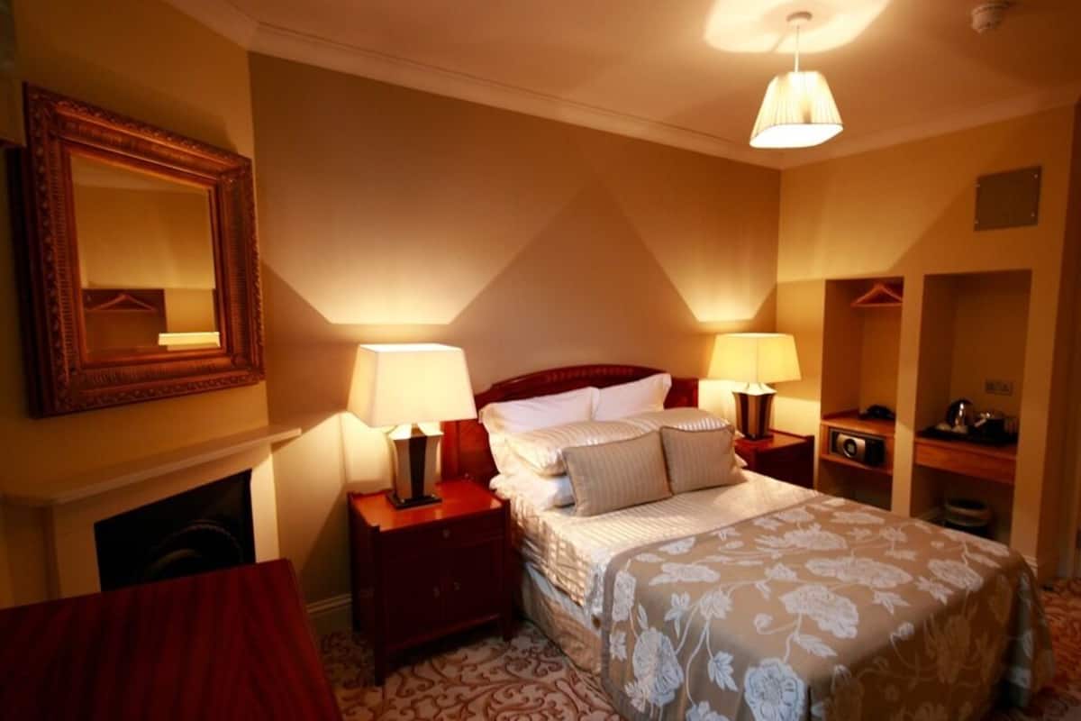 A hotel room with a large bed, two bedside tables with lamps, a mirror, a fireplace, and a wardrobe.