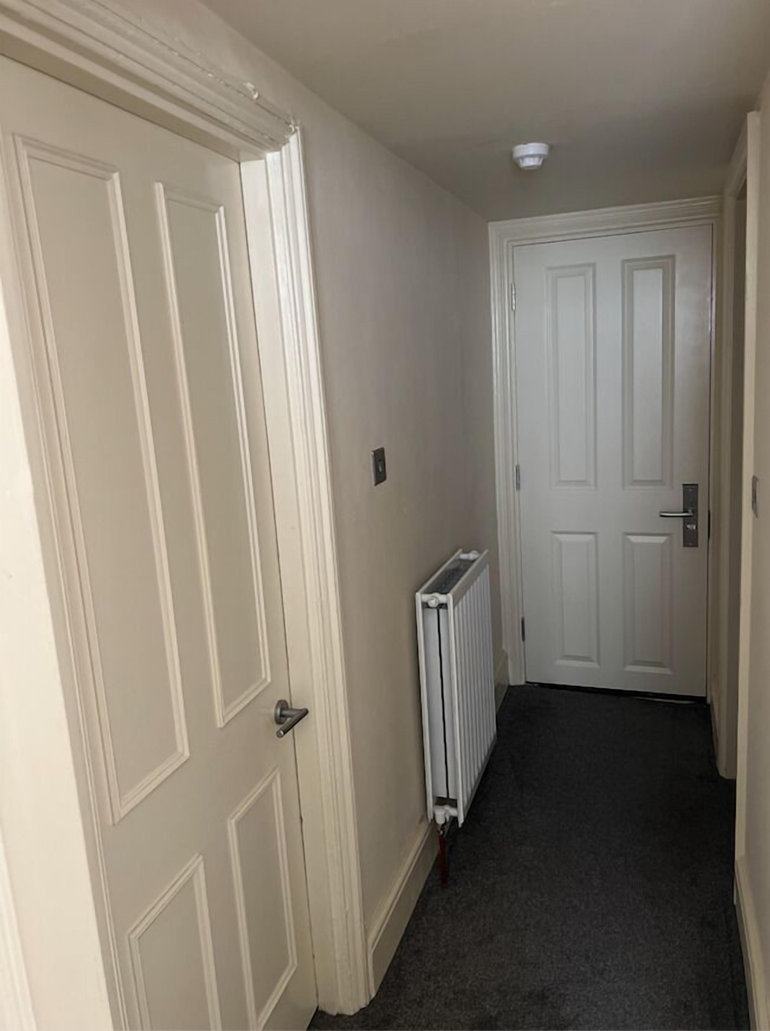 A narrow hallway with white doors and a radiator on the wall.