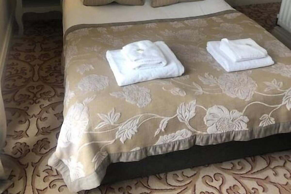 A neatly made bed with a floral-patterned bedspread, two pillows, and two folded towels on the bed.