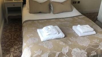 A neatly made bed with a floral-patterned bedspread, two pillows, and two folded towels on the bed.