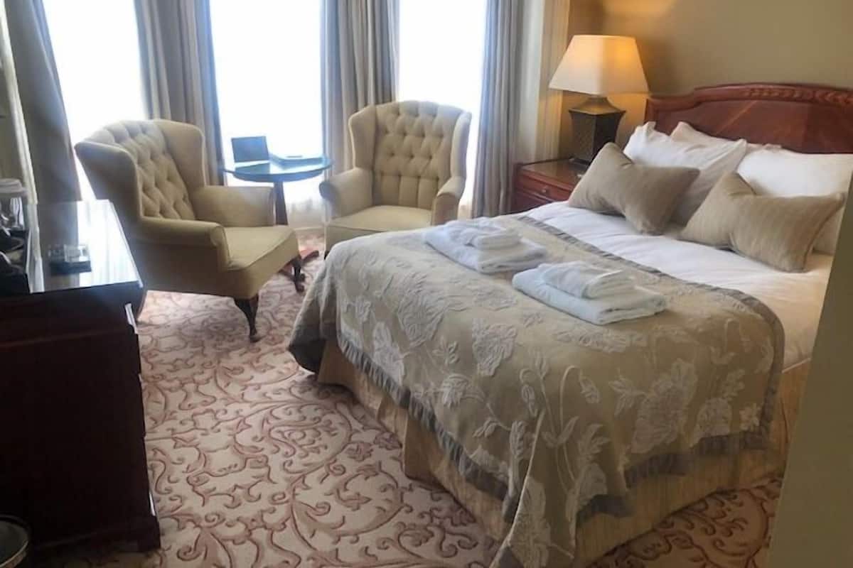 A hotel room with a large bed, two armchairs, a small table, and a lamp.