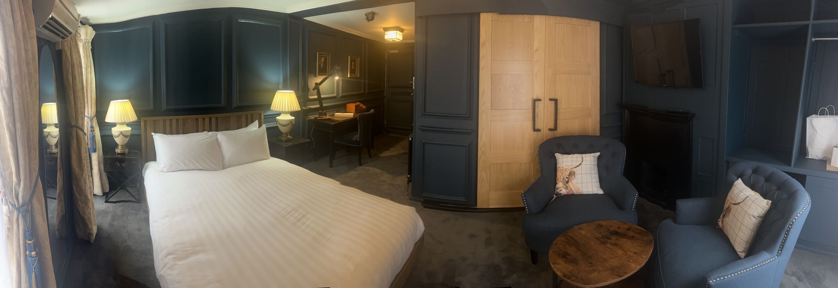 Ett hotellrum med en stor säng, ett skrivbord, en stol, ett litet runt bord och en garderob.