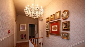 Ein Flur mit einer Chandelüster, gerahmten Bildern an der Wand und einem Feuerlöscher.
