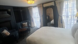 Ein Hotelzimmer mit einem großen Bett, einer Sitzecke mit Stuhl und kleinem Tisch, einer Wand-Klimaanlage und einem mit Vorhängen versehenen Fenster.