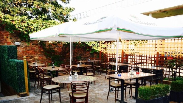Eine Terrasse im Freien mit runden Tischen und Stühlen, beschattet von einem weißen Sonnenschirm.