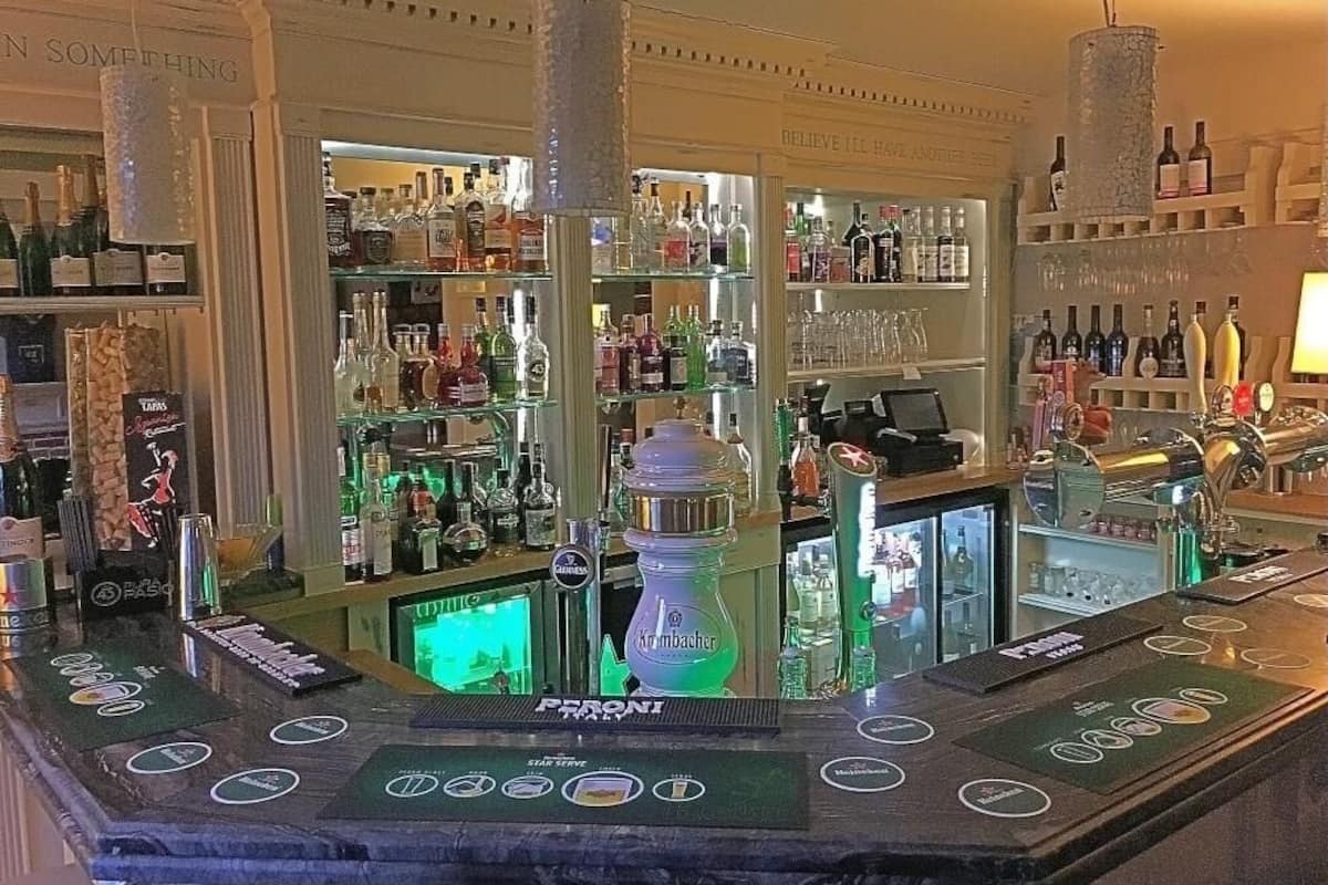 A bar area with a variety of liquor bottles, a water dispenser, and a bar counter with multiple taps.