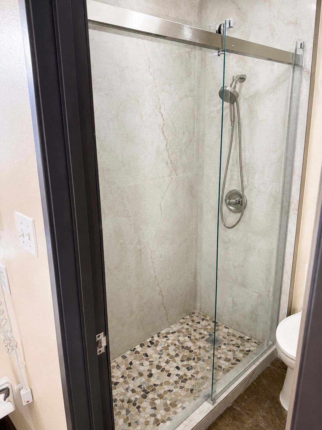 A glass-enclosed shower with a tiled floor, a showerhead, and a control panel.
