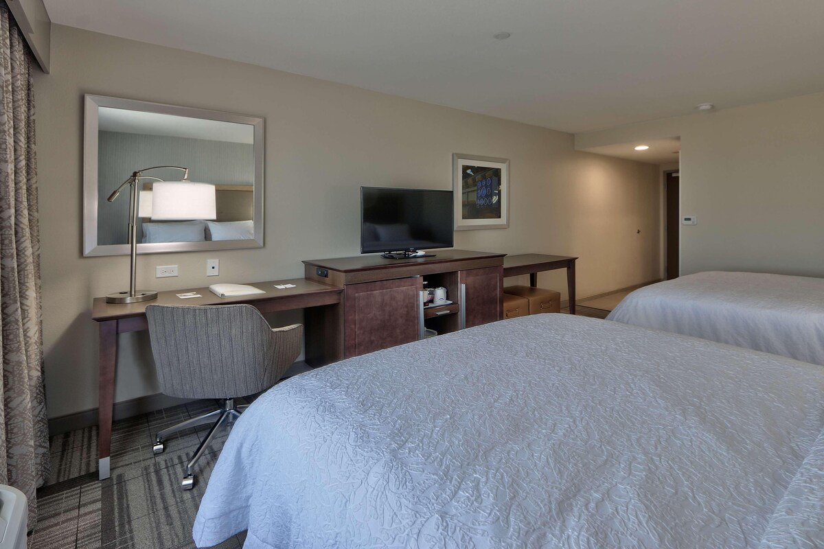 Une chambre d’hôtel avec deux lits, un bureau avec un ordinateur, une télévision et un miroir.