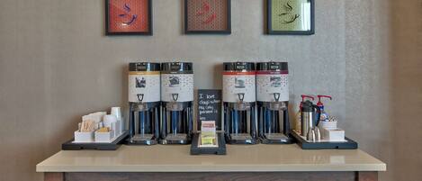 A coffee station with multiple coffee machines, a tray with cups and a sign, and framed artwork on the wall.