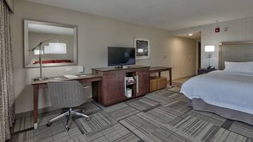 A hotel room with a bed, desk, chair, television, and a large mirror.