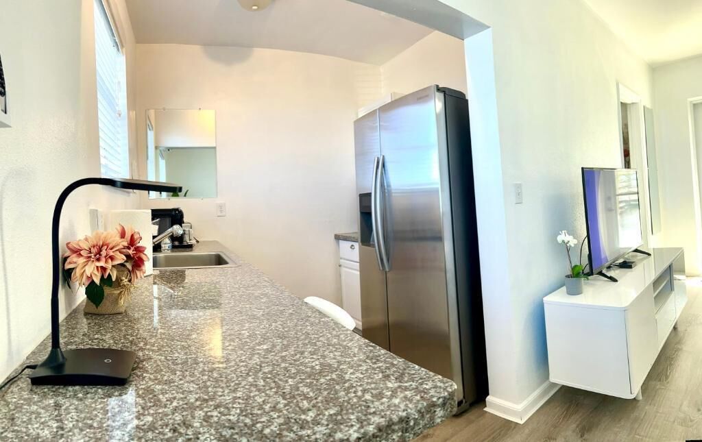 Cozinha moderna com bancadas de granito, geladeira de aço inoxidável e armário branco.