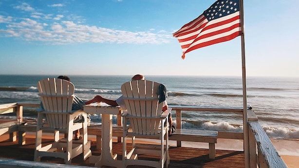 Two Adirondack chairs on a wooden deck overlooking the ocean with an American flag. - A1A Ocean Club (Flagler Beach)