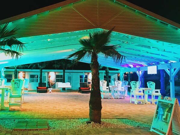 An outdoor seating area with palm trees, covered by a roof, and white chairs. - A1A Ocean Club (Flagler Beach)