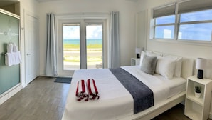 A hotel room with a bed, a nightstand, a lamp, a potted plant, and a view of the beach. - A1A Ocean Club (Flagler Beach)