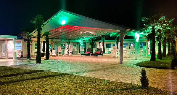 Uma área externa coberta com assentos e palmeiras, provavelmente parte de um hotel ou resort.