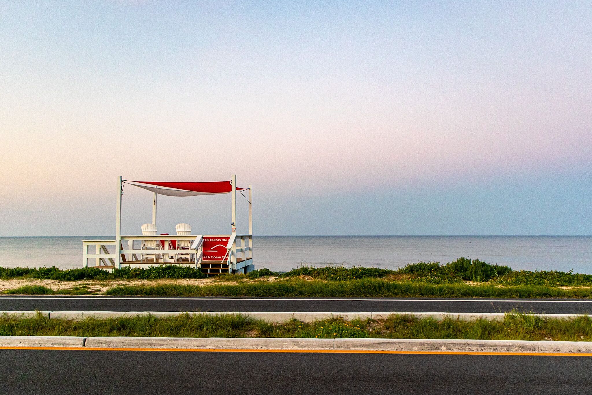 A beachside kiosk with a red canopy, white chairs, and a sign indicating it is for guests only.