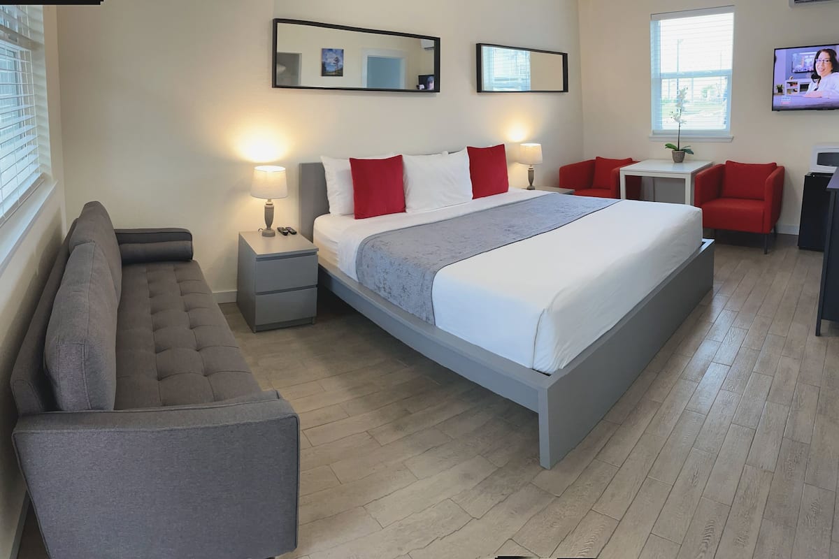 A modern hotel room with a large bed, bedside tables, a sofa, and a TV.