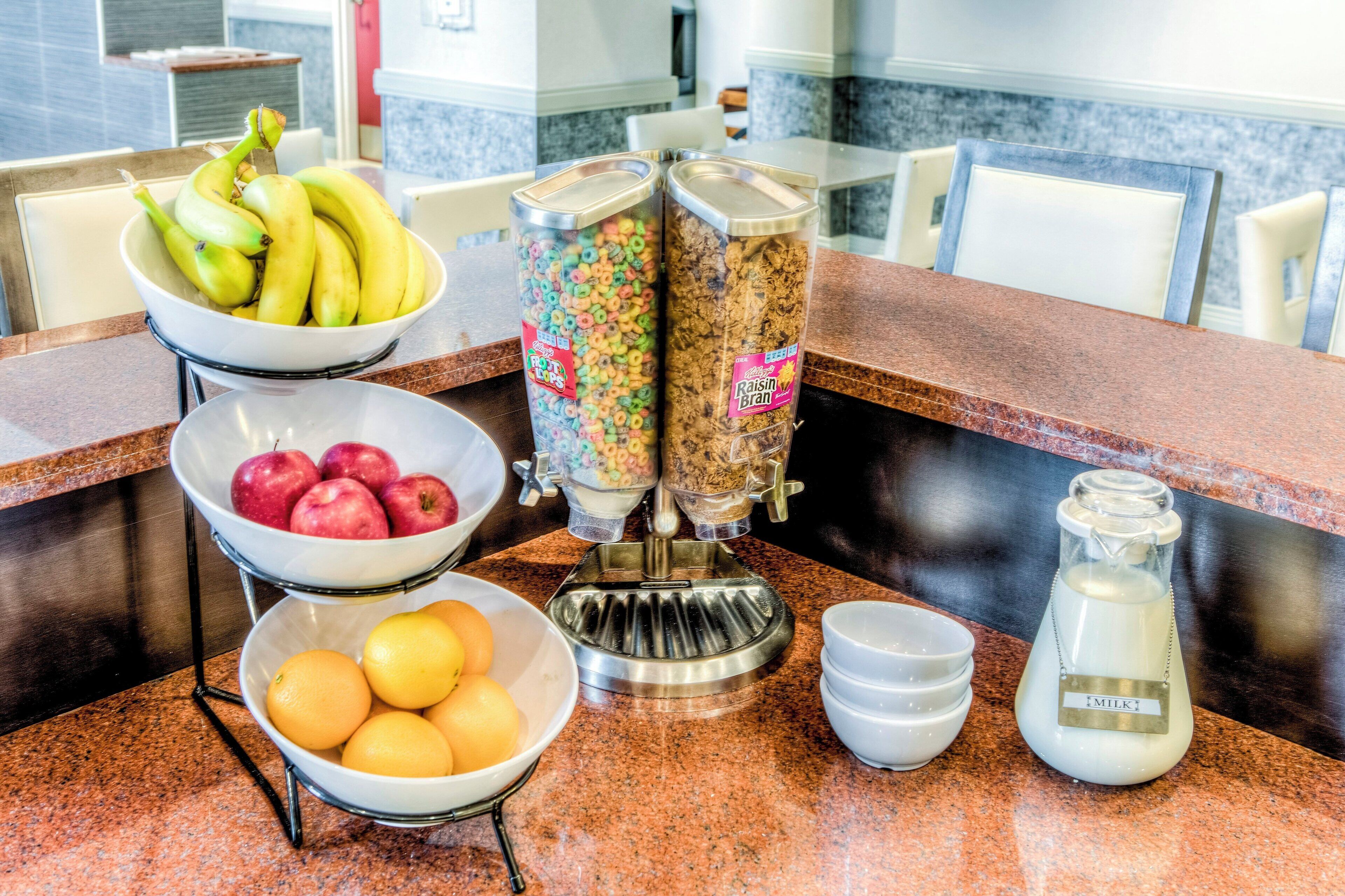 Balcão de café da manhã com tigelas de frutas, dispensadores de cereais e um dispensador de leite.