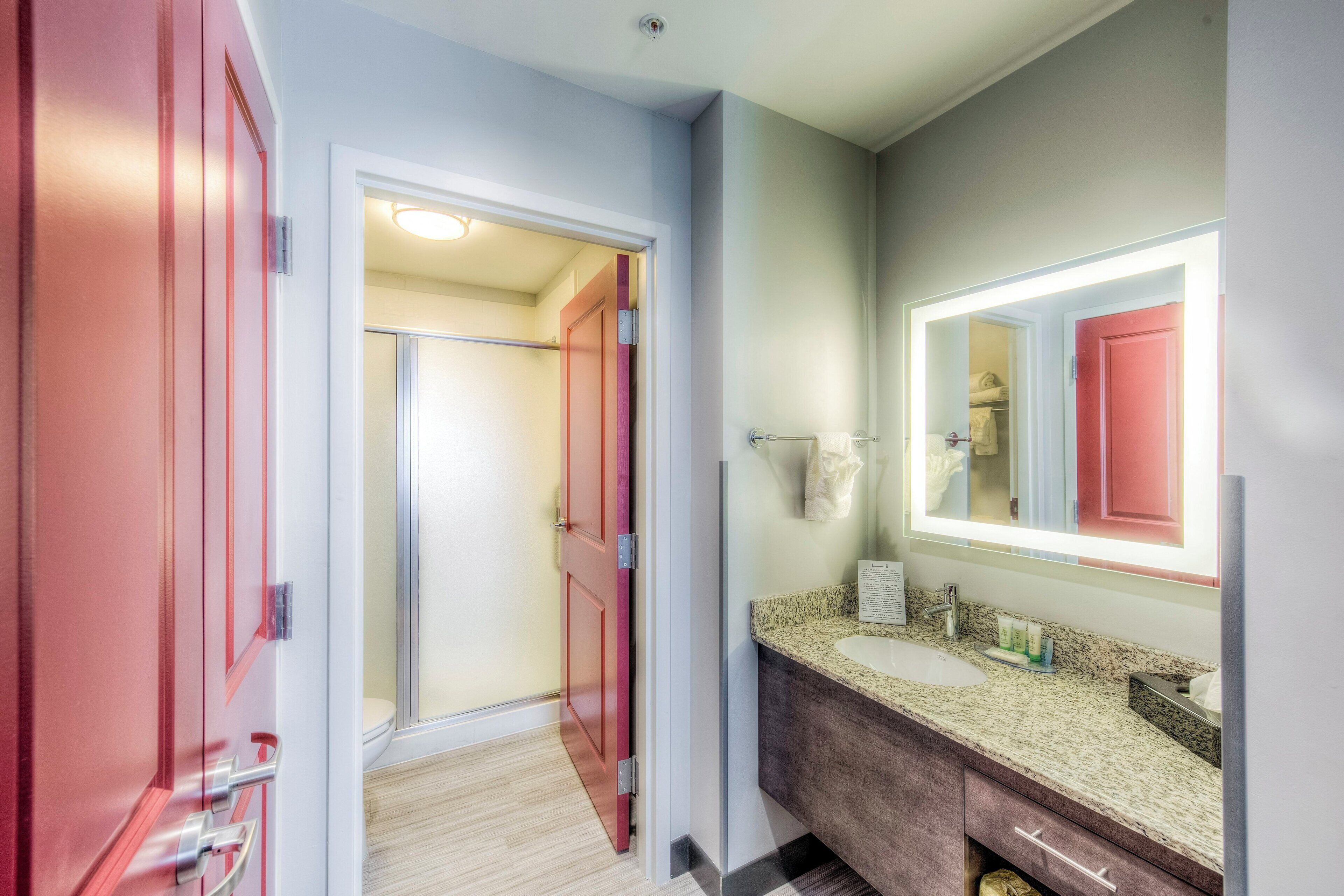 A bathroom with a sink, mirror, and red door.