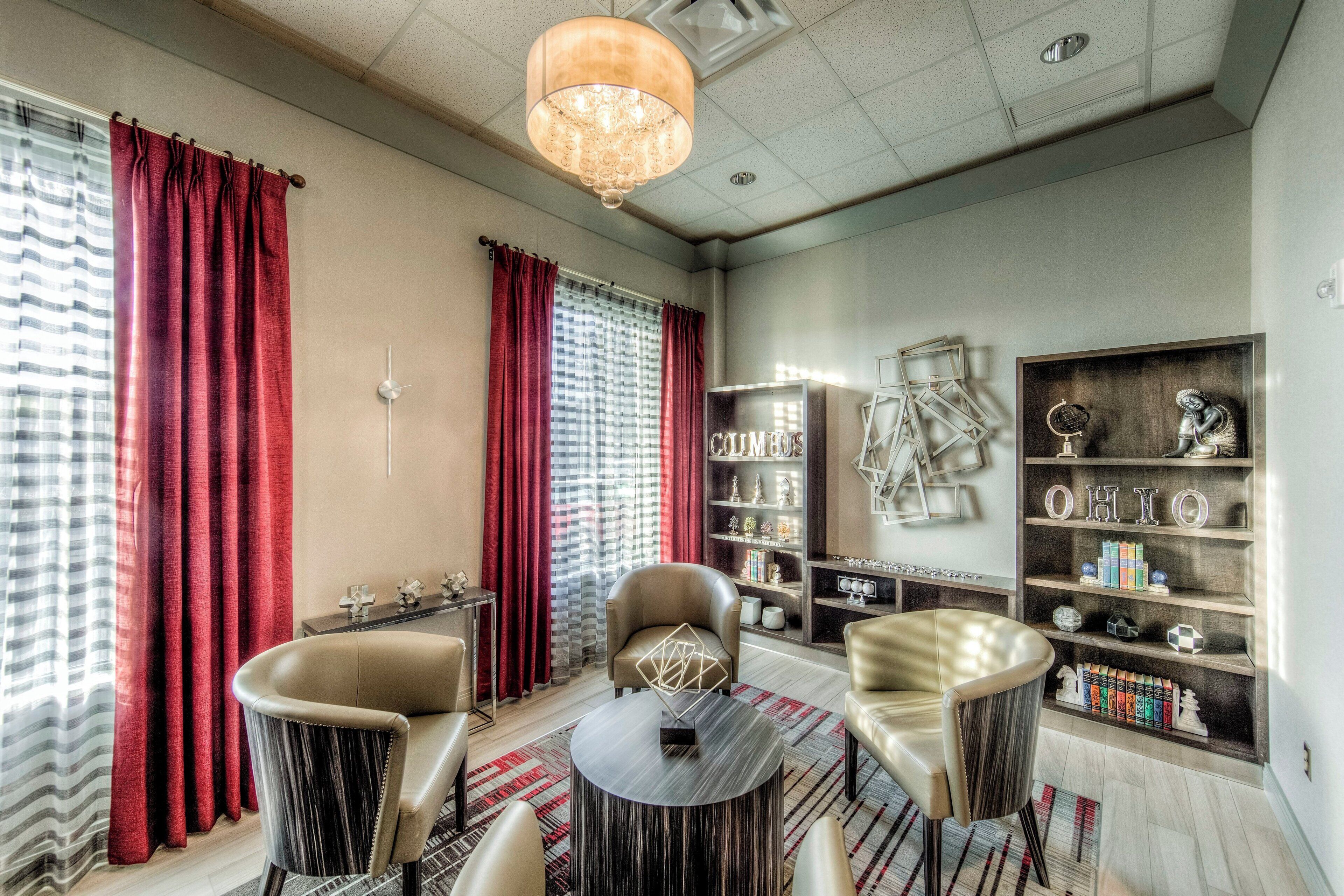 A modern living room with a chandelier, leather chairs, a round coffee table, and a bookshelf.