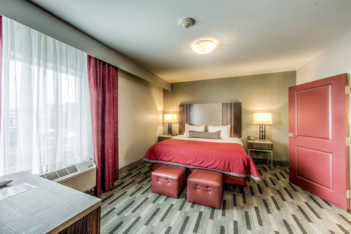 A hotel room with a bed, bedside tables, a desk, and a window with curtains.