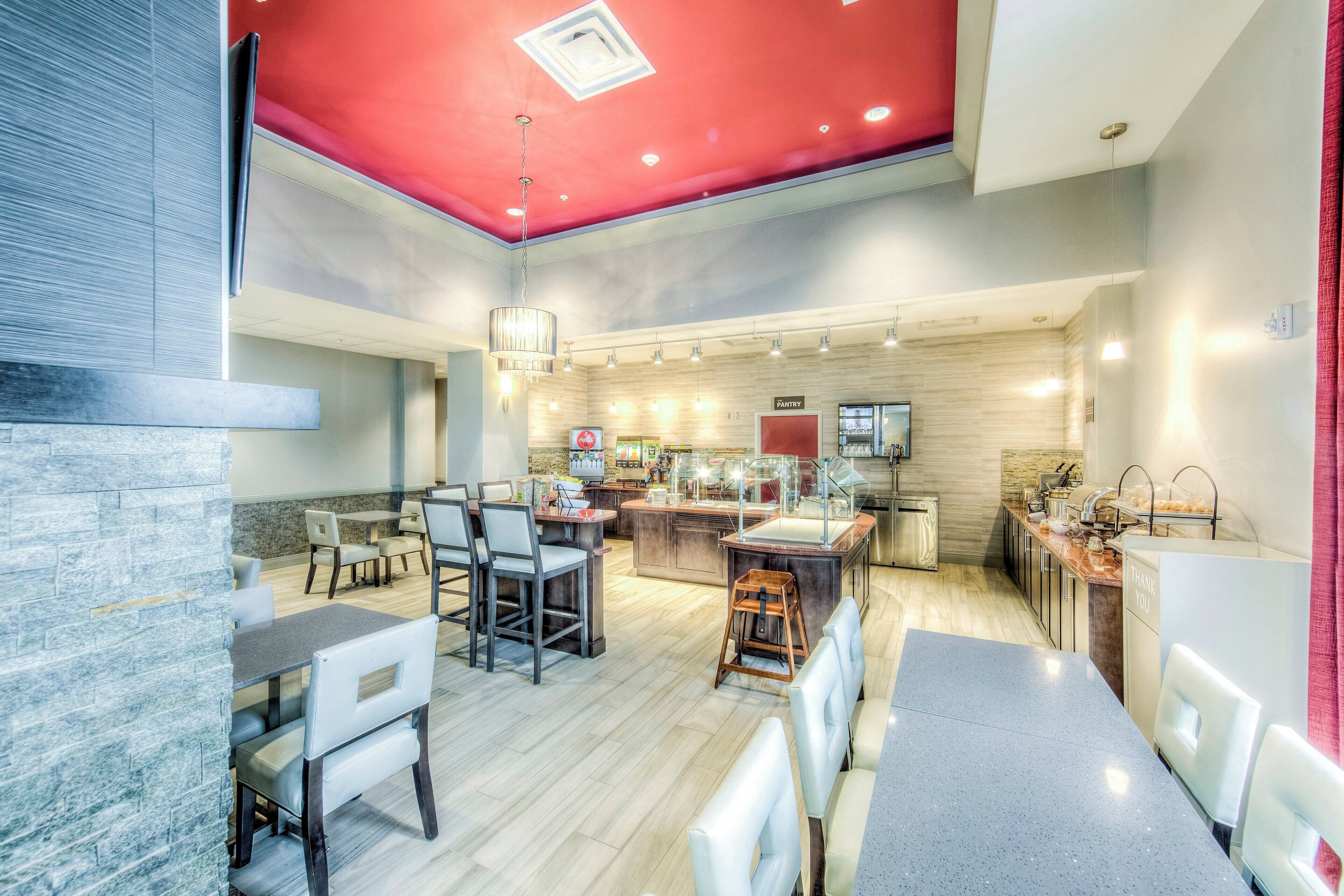 A modern restaurant with a red ceiling, a dining area with tables and chairs, a kitchen area, and a sign indicating a pantry.