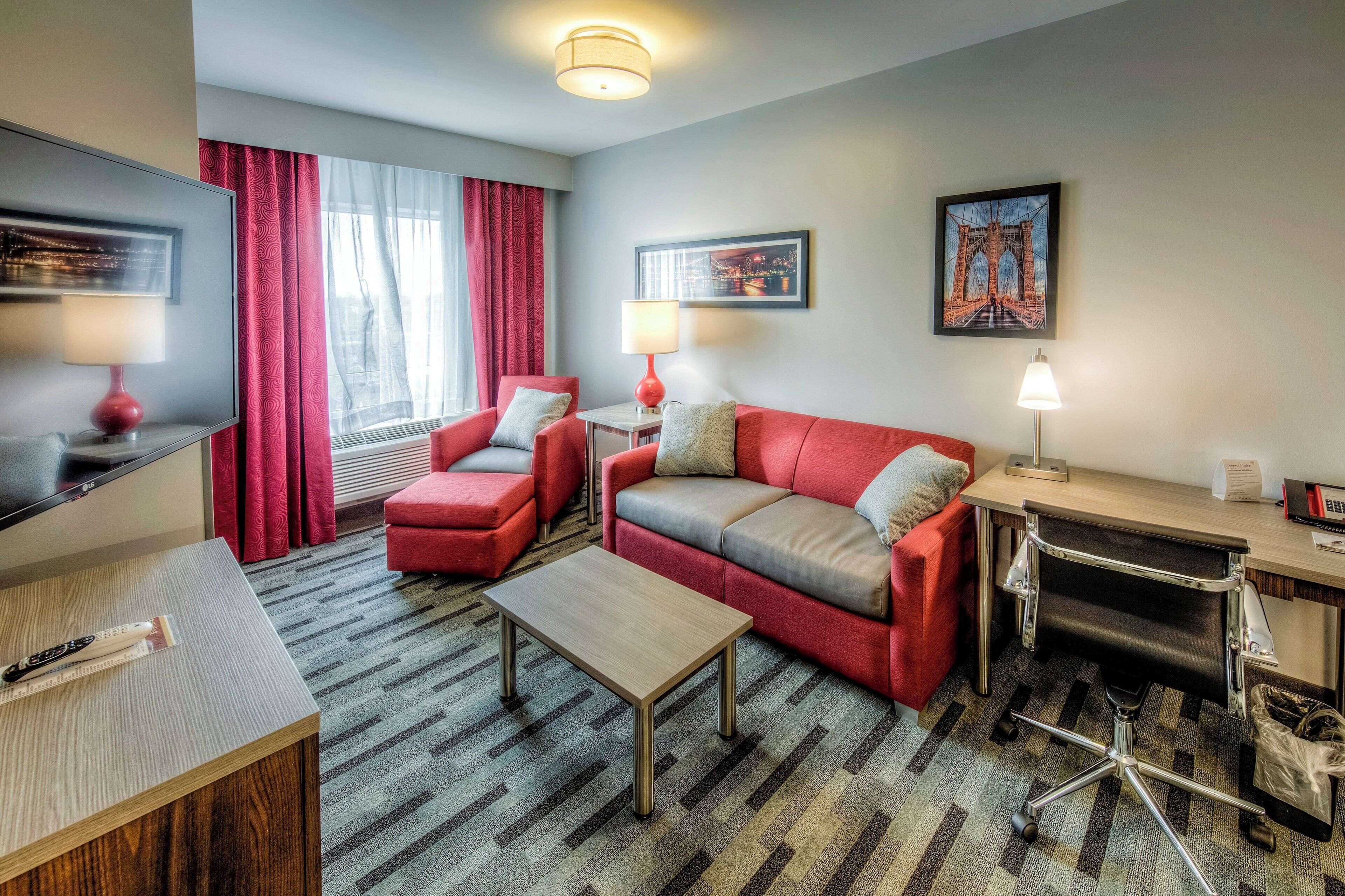 Habitación de hotel con sofá, sillón, escritorio y vistas a un puente.