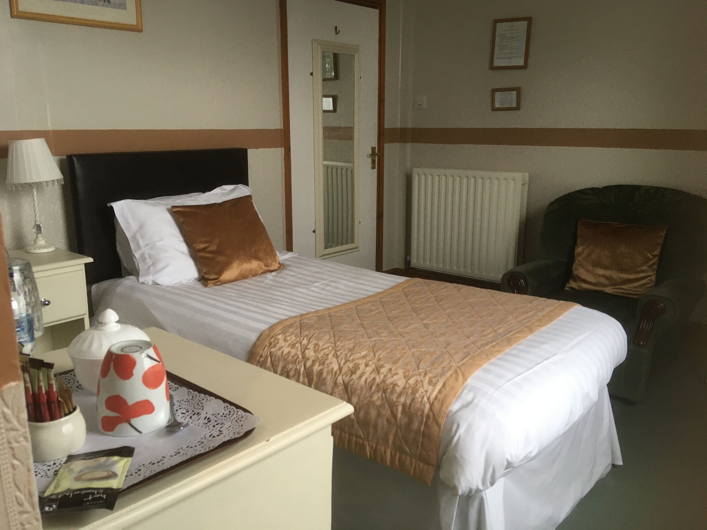 A neatly arranged hotel room with a bed, a chair, a bedside table with a lamp, and a radiator.