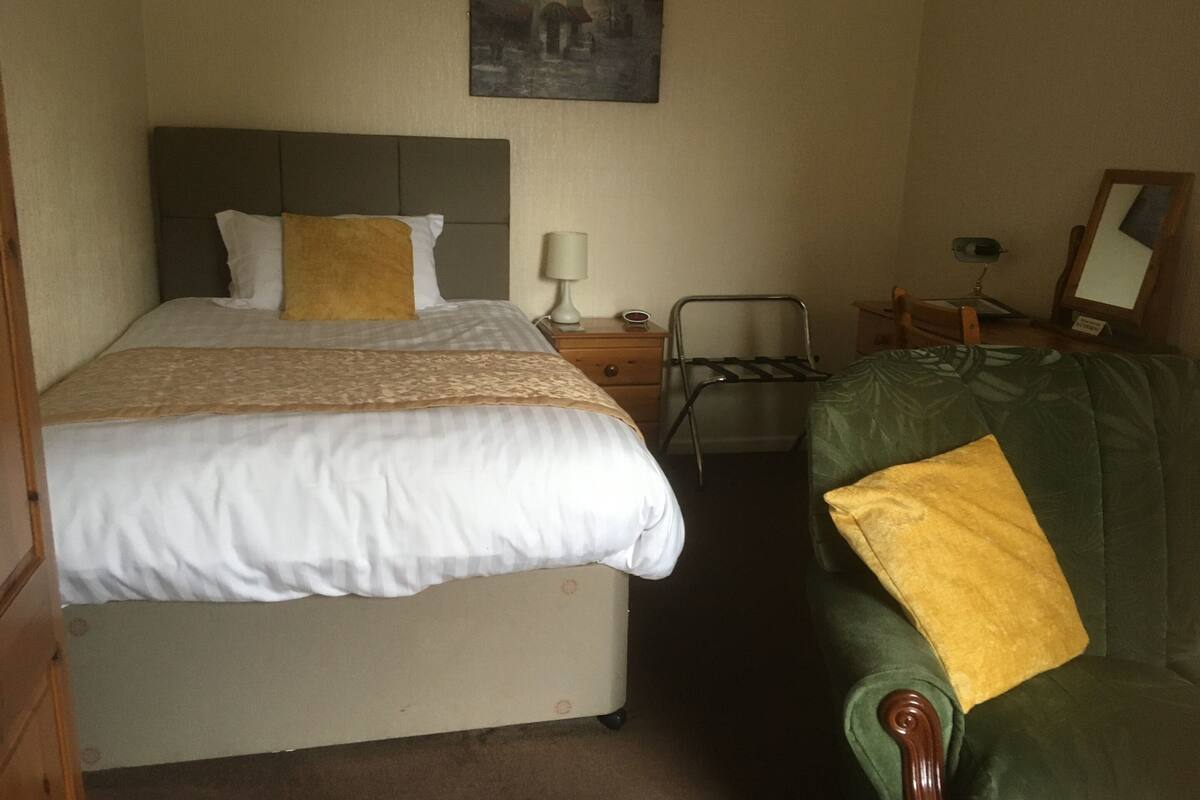 A hotel room with a bed, a chair, a nightstand, a lamp, and a painting on the wall.