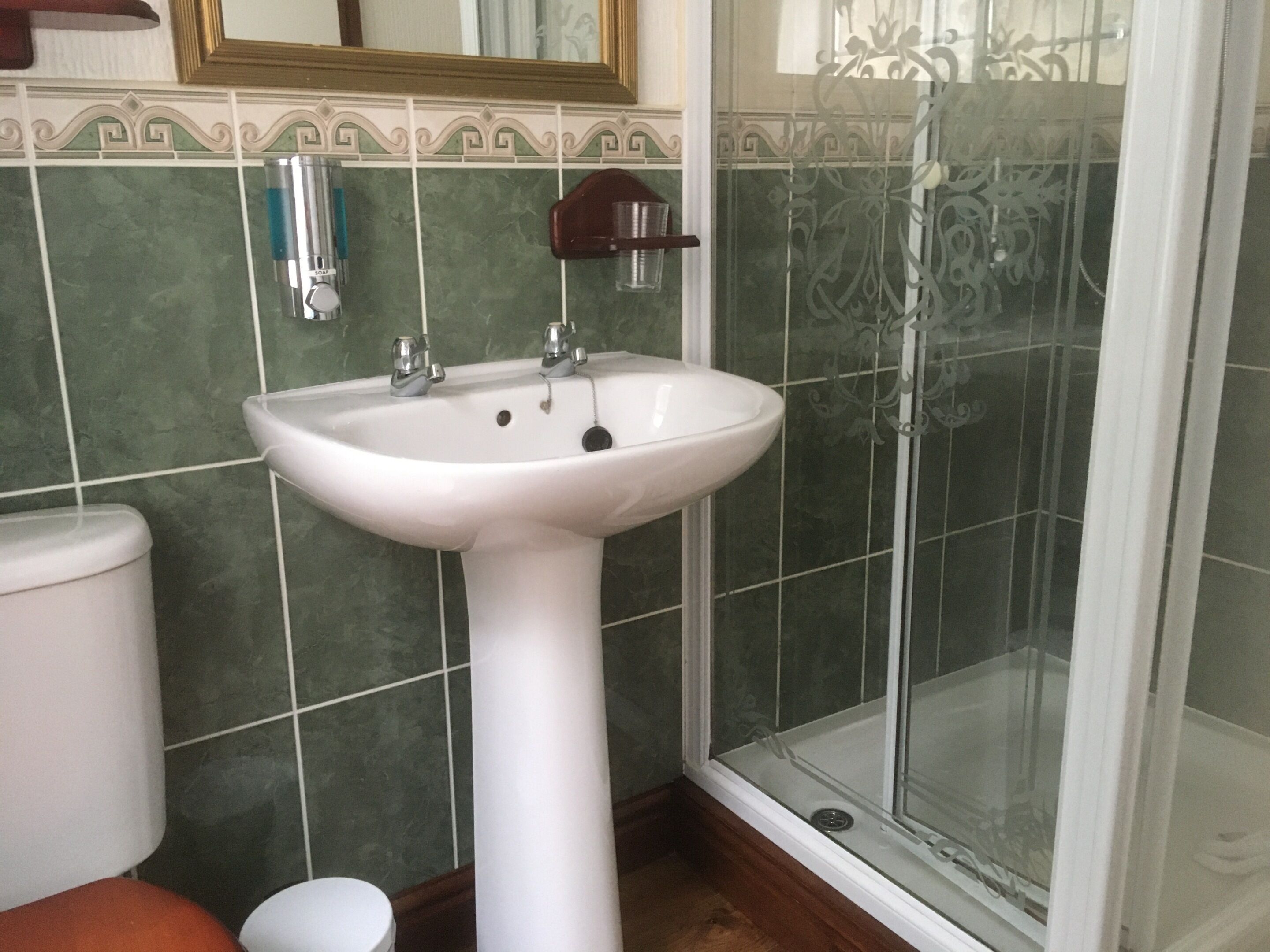A bathroom with a white pedestal sink, a toilet, and a glass shower enclosure.