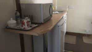 Une cuisine compacte équipée d’un four à micro-ondes, d’un petit évier et d’un réfrigérateur. On y trouve un plan de travail en bois avec une bouilloire, une bouteille d’eau et un récipient blanc.