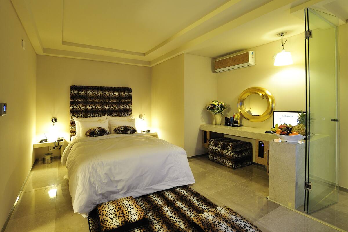 A modern hotel room with a large bed, a vanity with a mirror, and a glass shower enclosure.