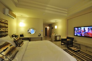 A hotel room with a large bed, a television, a desk with a chair, and a small table with a mirror and decorative items.