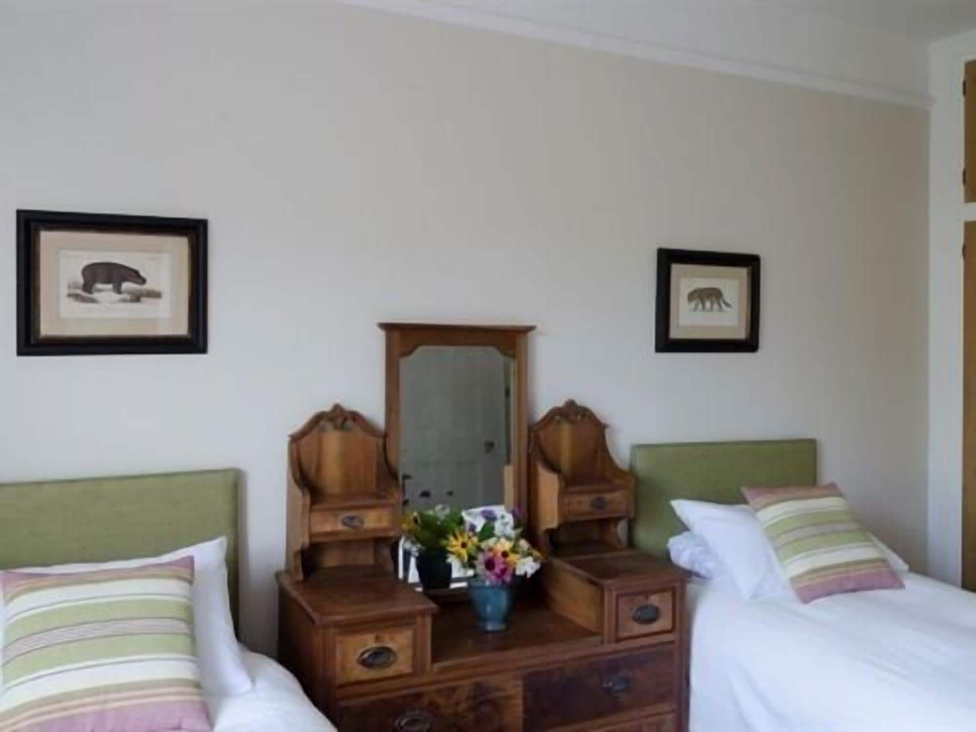 A room with two beds, a dresser with a mirror, and two framed animal pictures on the wall.