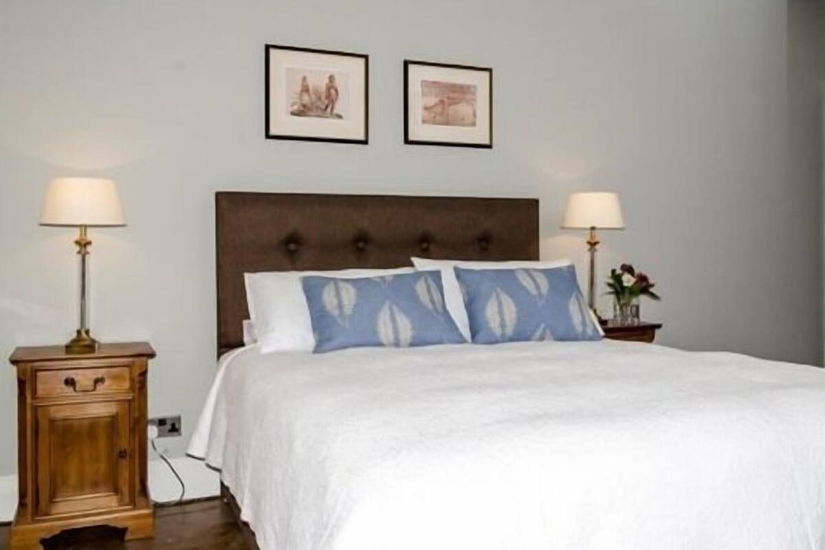 Quarto com uma cama grande, duas mesas de cabeceira e duas luminárias fixadas na parede.
