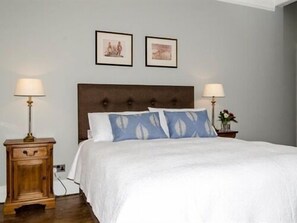 A bedroom with a large bed, two bedside tables, and two wall-mounted lamps. - The Lions (Newark)