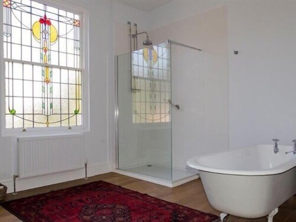 Un baño con cabina de ducha de vidrio, una bañera blanca y un ventanal de vitral.