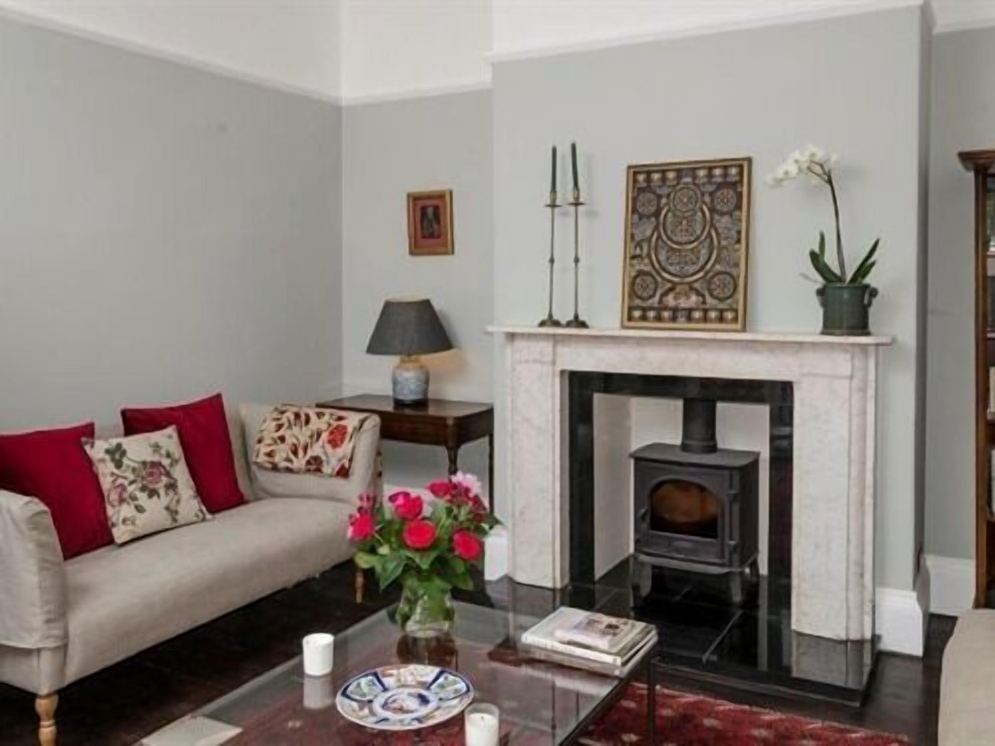 Una sala de estar con un sofá, una chimenea, una mesa con un florero y una lámpara.