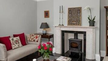 Una sala de estar con un sofá, una chimenea, una mesa con un florero y una lámpara.